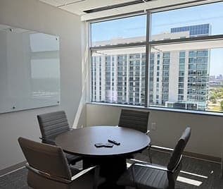 A conference room with a round table, glass whiteboard and a window overlooking Frisco