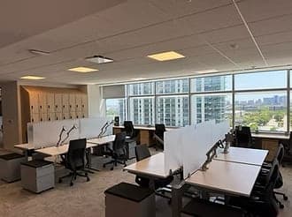 Desks with monitors and privacy dividers beside a wall of windows looking over Frisco